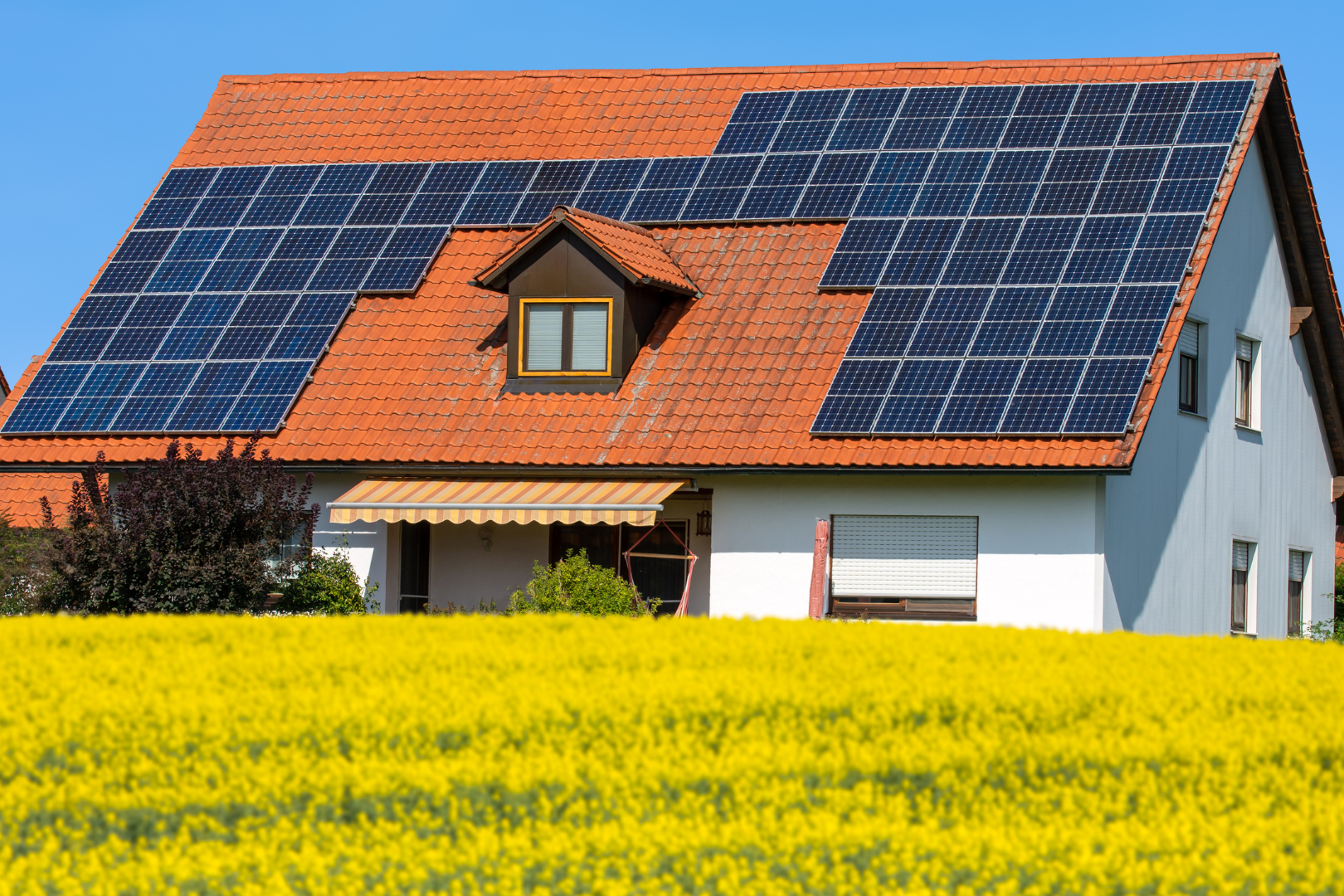 Villa con tetto rosso con pannelli fotovoltaici, prato di fiori gialli. Incentivi fotovoltaico residenziale