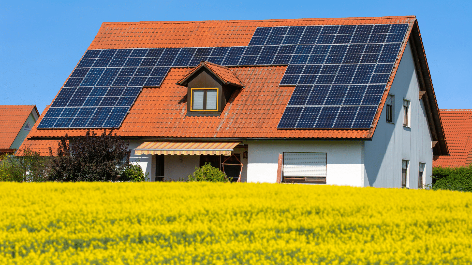 Villa con tetto rosso con pannelli fotovoltaici, prato di fiori gialli. Incentivi fotovoltaico residenziale