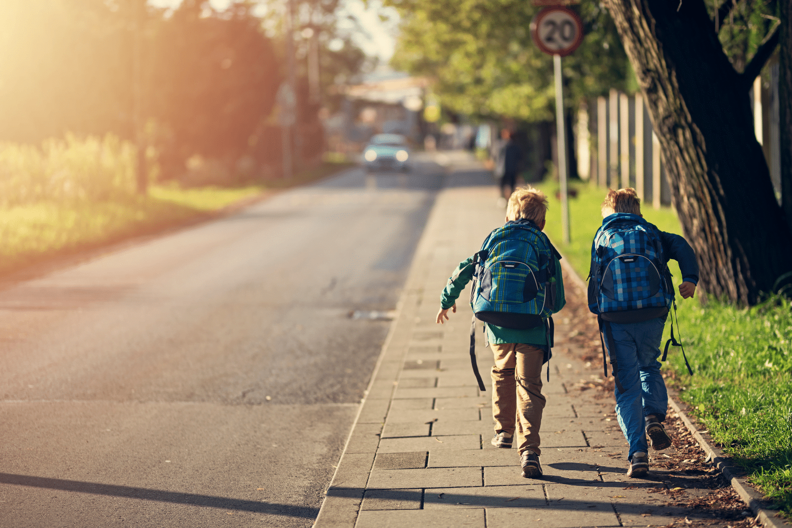 Bambini che vanno a scuola che corrono su marciapiede di strada pubblica, con cartello stradale. Spazio verde e auto che percorre la strada. Contributi a fondo perduto per interventi di efficientamento energetico.